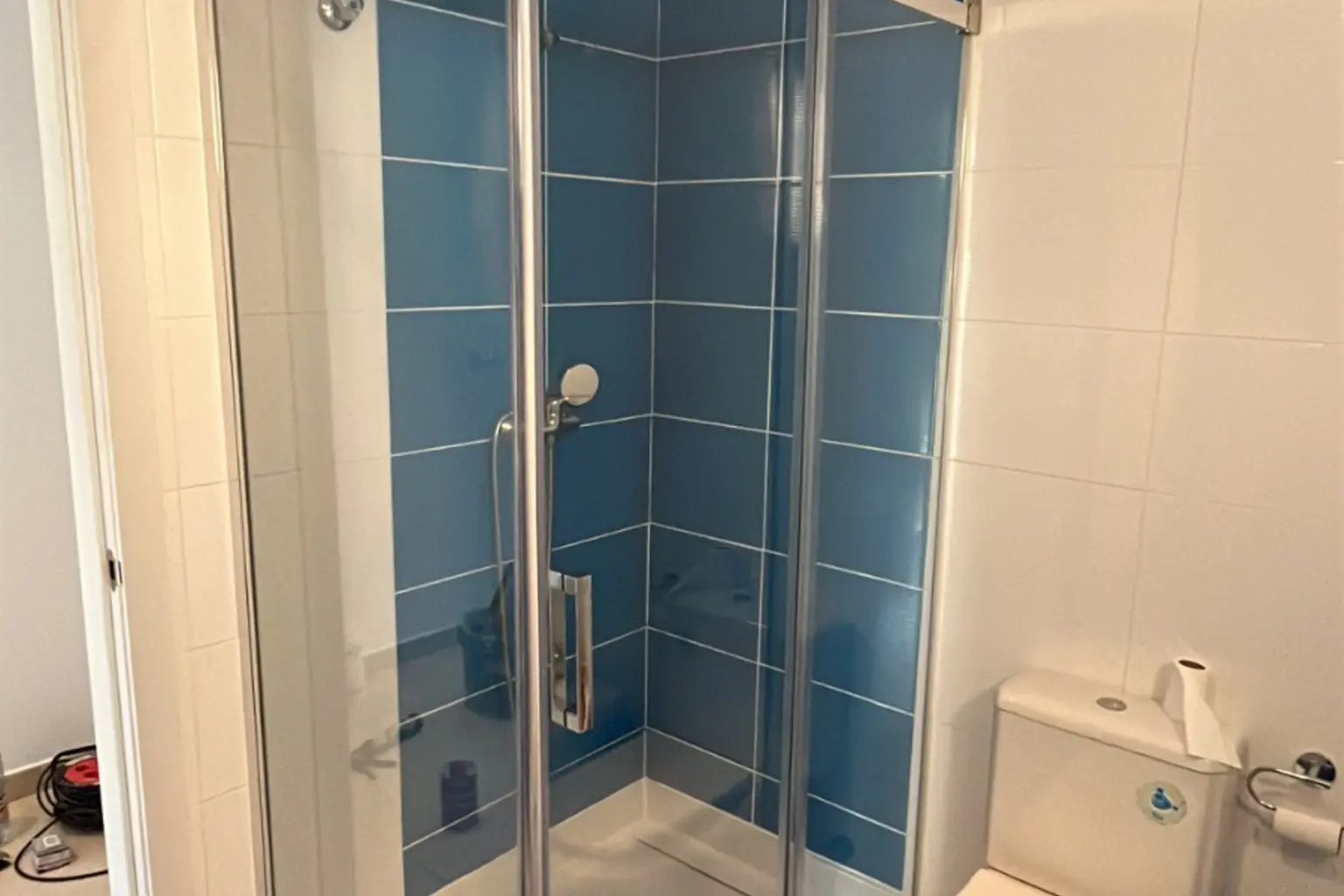 Mampara de ducha angular en un baño alicatado en azul